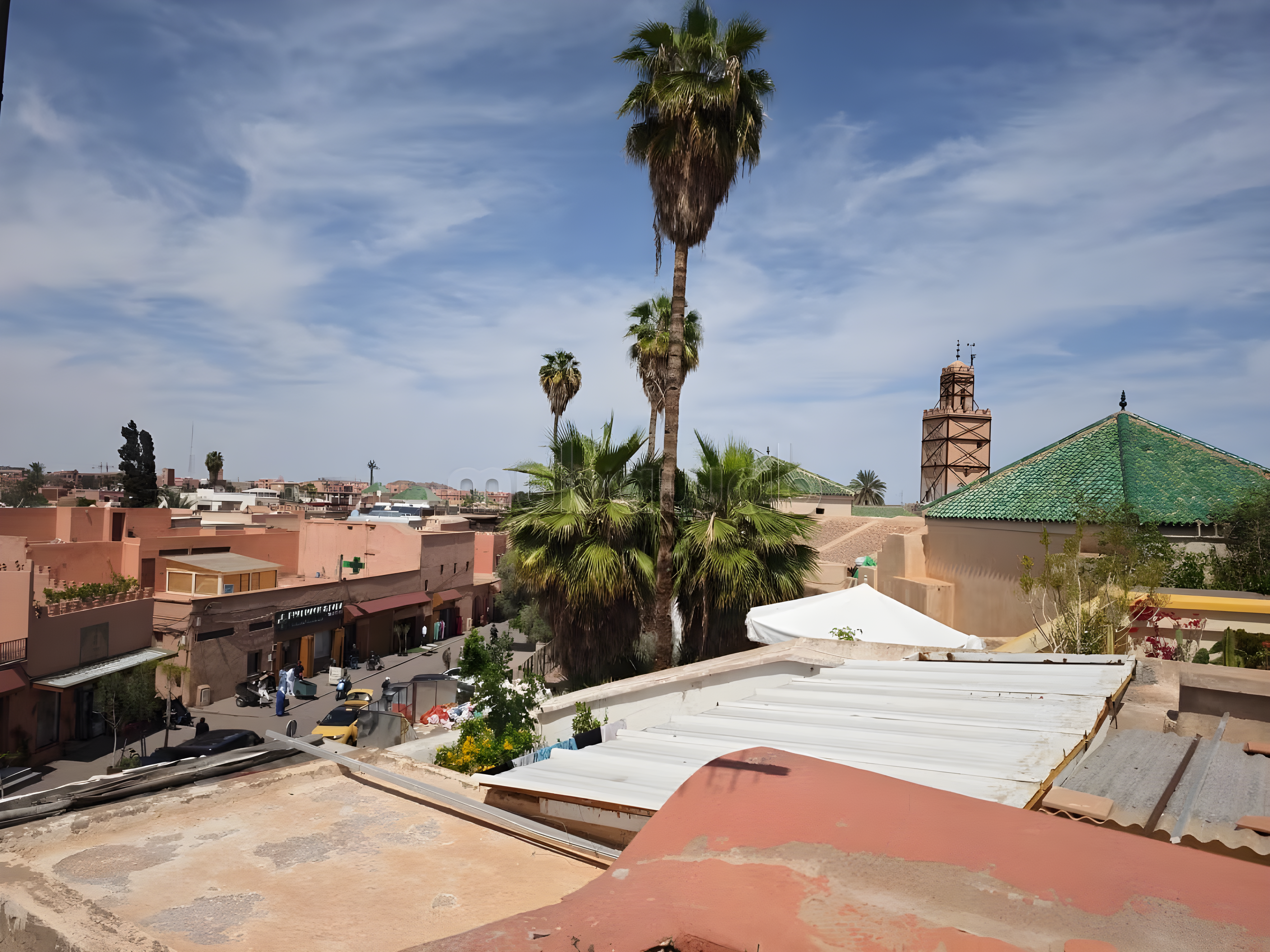 Rooftop of Rmila guesthouse with Moroccan green-tiled roof and cityscape view.