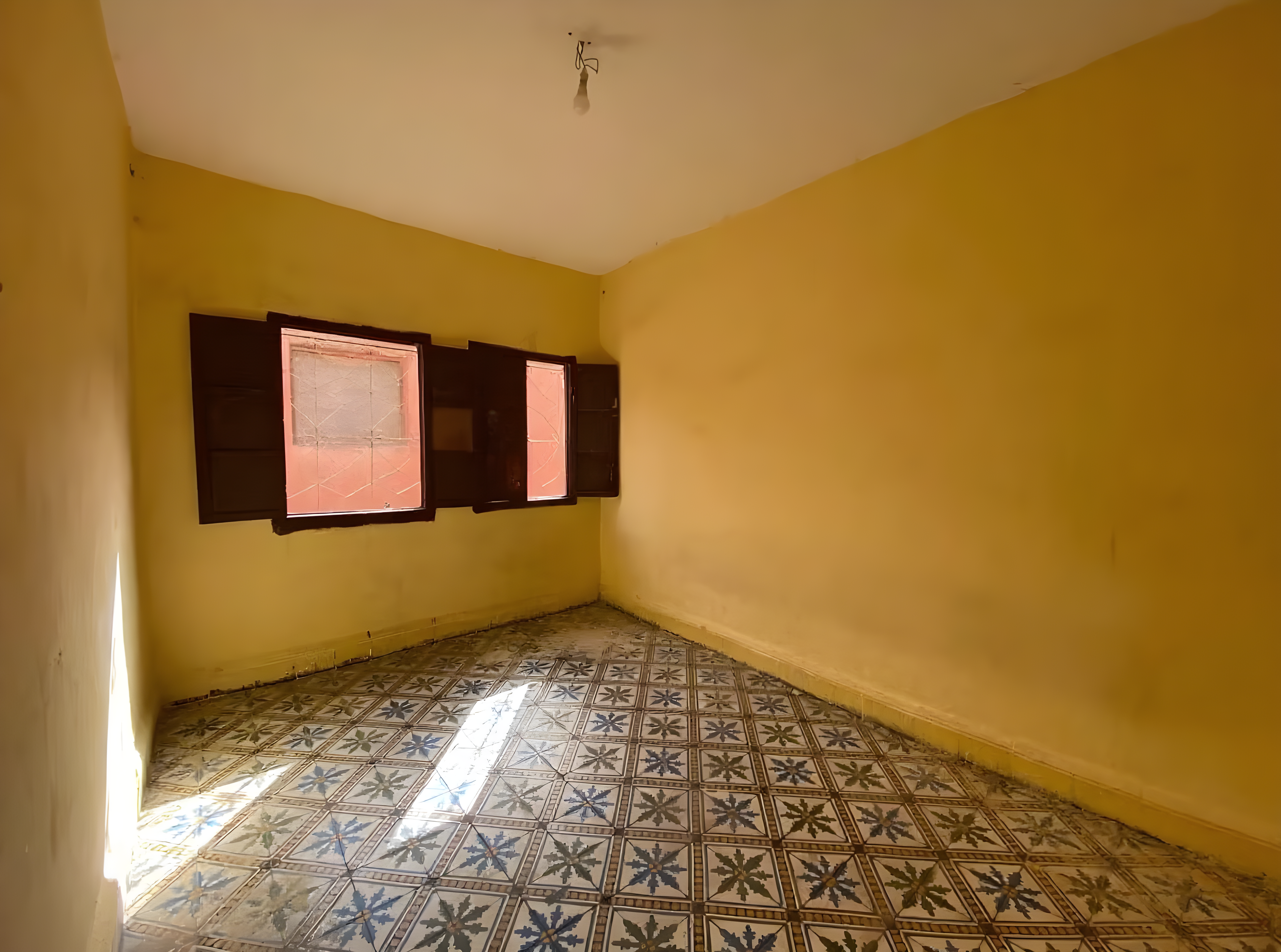 Yellow-walled bedroom with tiled floors and wooden shuttered windows.