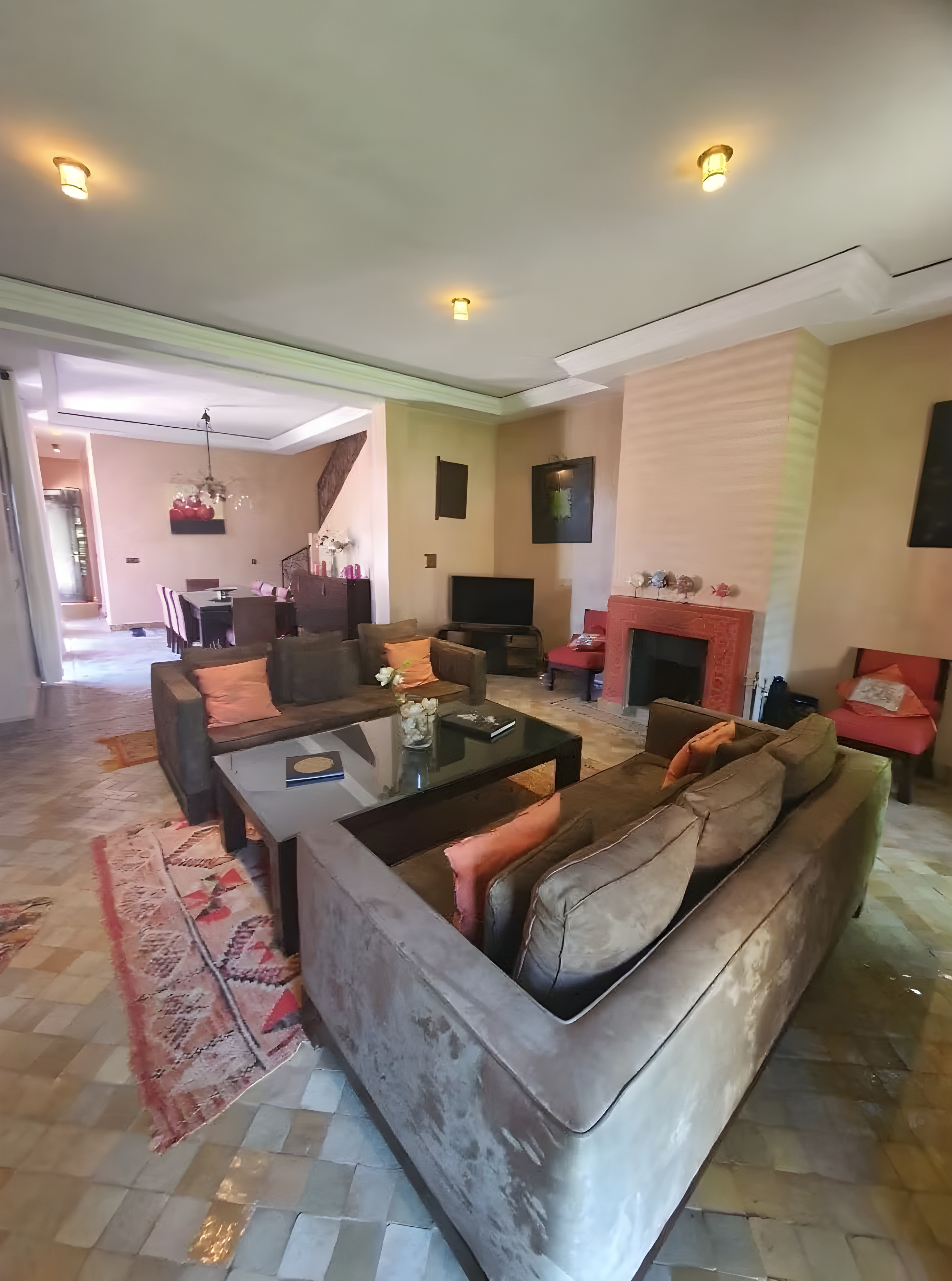 Salon in Ennakhil riad with couches, coffee table, tiled floor, and warm lighting.