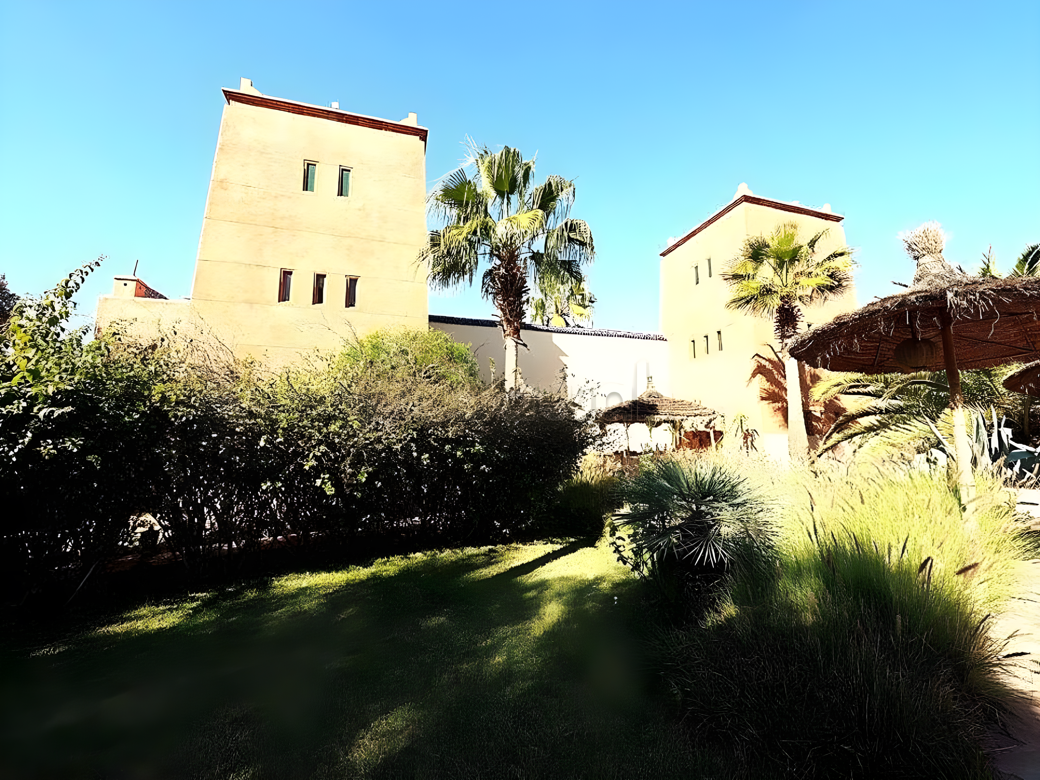 Guesthouse facade on Route Amizmiz with sand-colored buildings and palm trees.