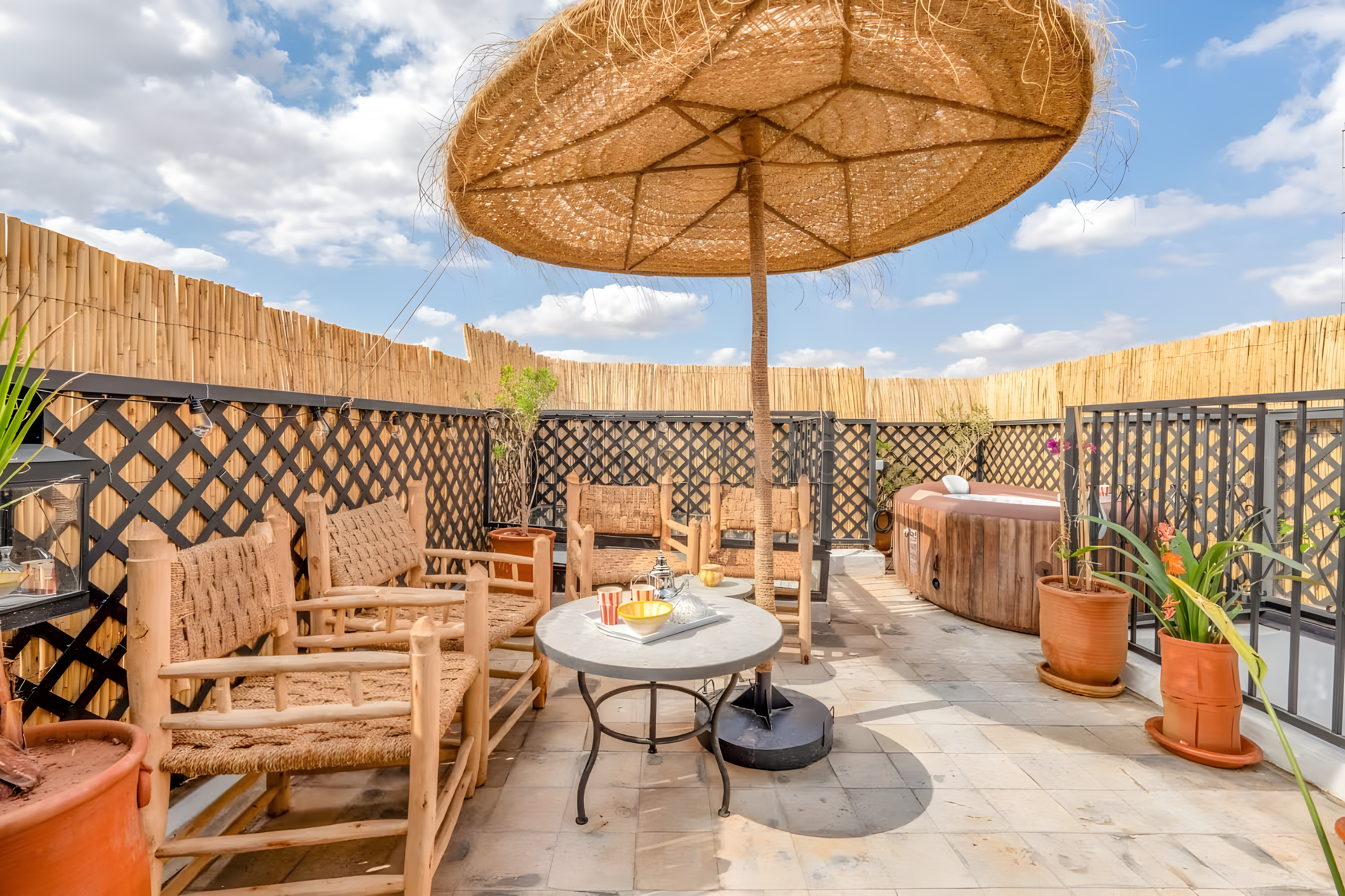 Rooftop with straw parasol, hot tub, woven chairs, and potted plants in Michouar.