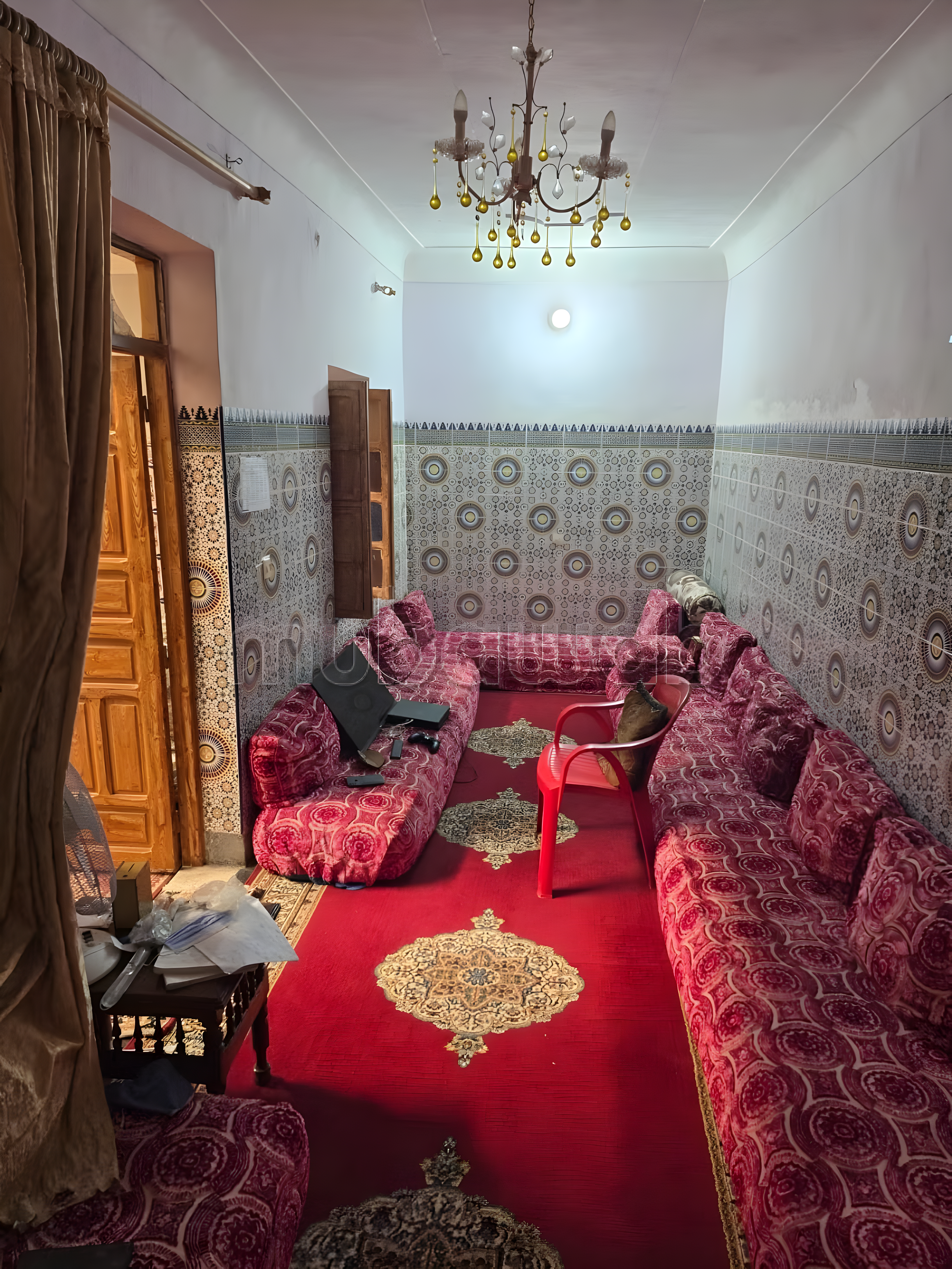 Marokkanischer Salon in Zaouia Sidi Ghalem mit gemusterten Wänden und rotem Teppich.