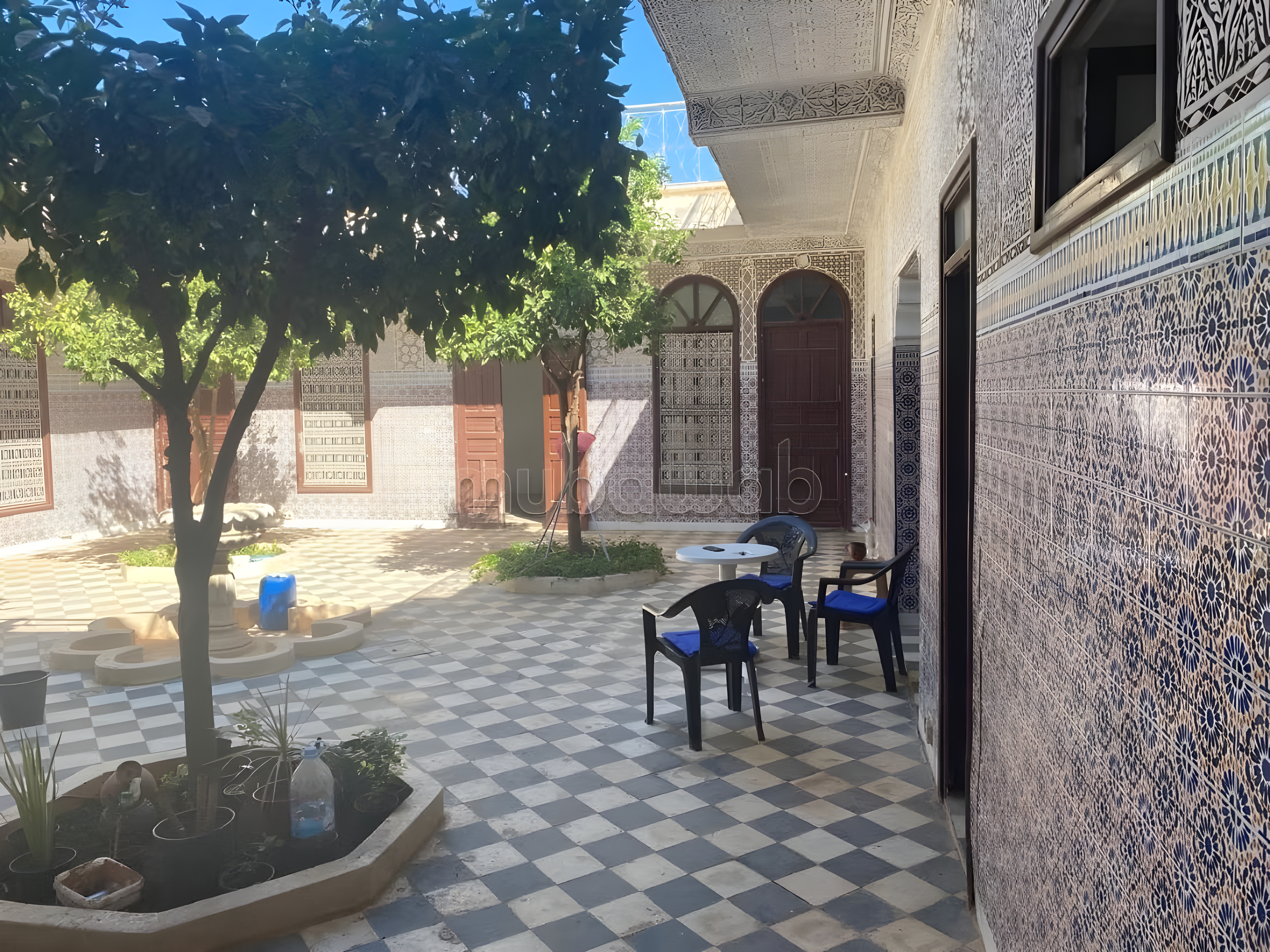 Courtyard with tiled flooring, mosaic walls, and a central tree planter in Ennakhil guesthouse.