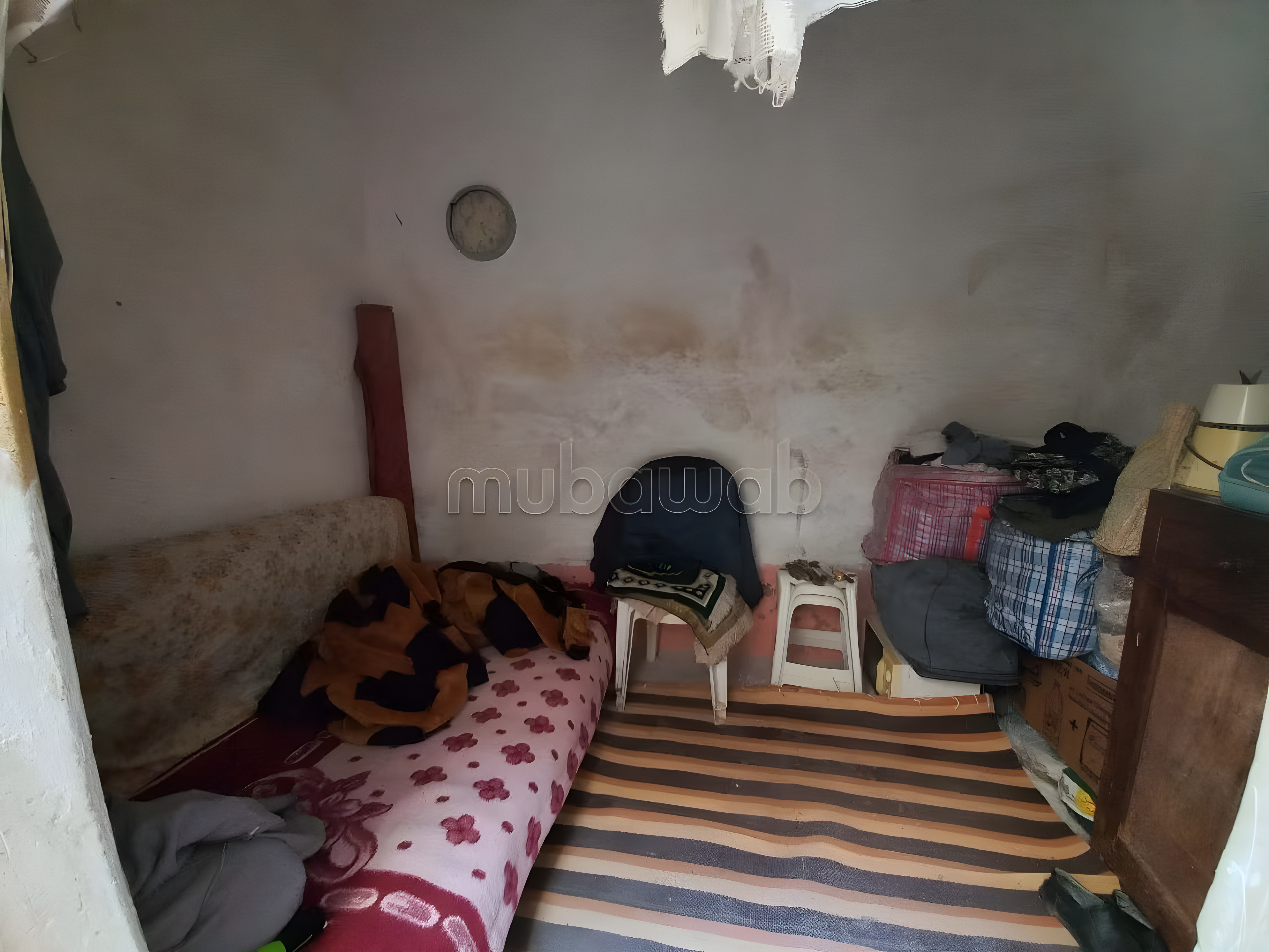 Modest guesthouse bedroom in Ksibat Nhas with simple furniture and personal items.